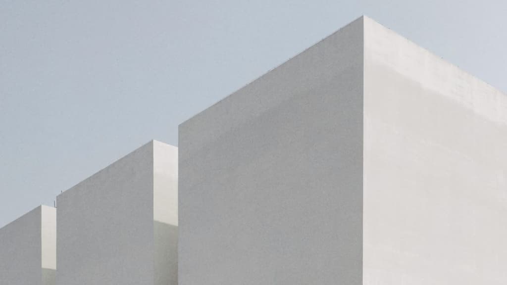 Three plain white building blocks in a row, stepping down in size, against a pale sky
